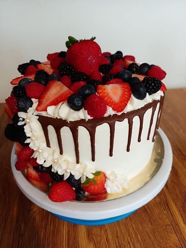 White buttercream cake with chocolate drip and overflowing fresh berries