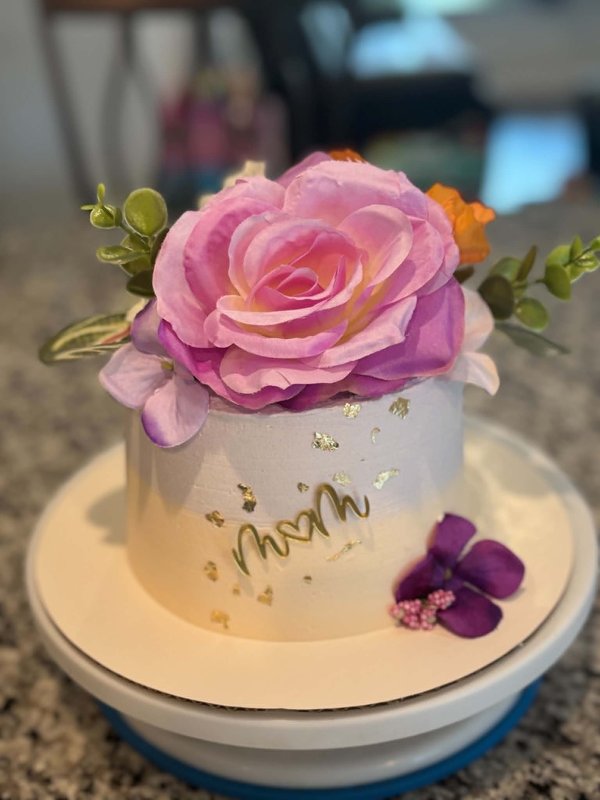 White buttercream cake with large silk flowers, gold leaf, and a teal butterfly