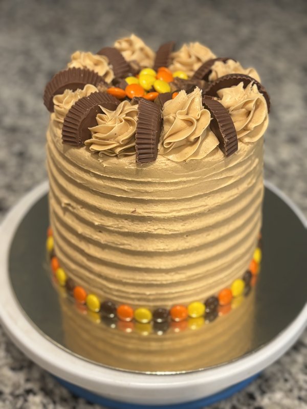Tall peanut butter buttercream cake topped with Reese's cups