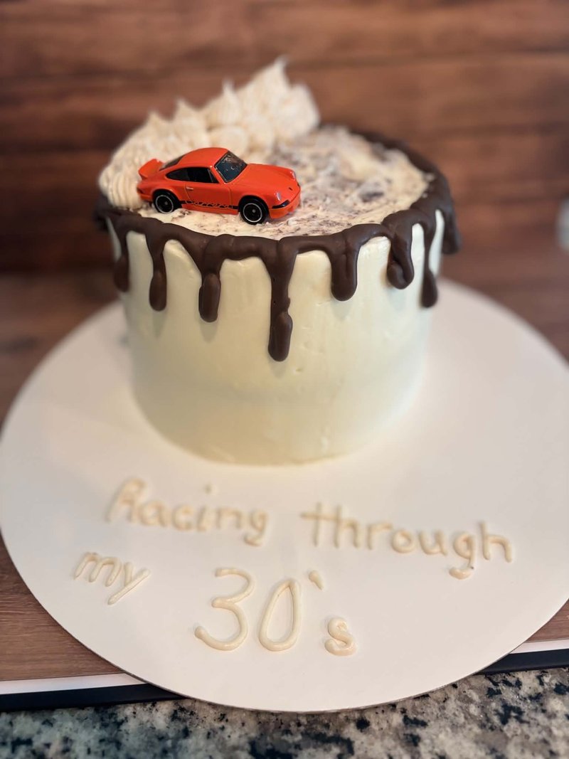 White buttercream cake with chocolate drip and a red sports-car topper, gold "Racing through my 30's" lettering on the cake board