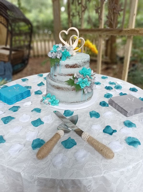 Two-tier wedding cake with teal drip and roses set on a wood table