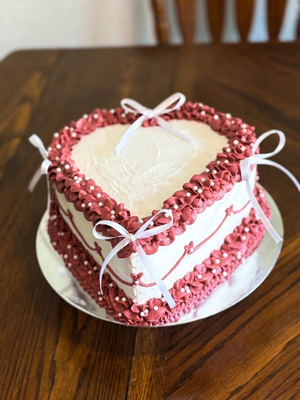 Heart-shaped cake with dusty rose ruffle piping, pearl dots, and white ribbon bows